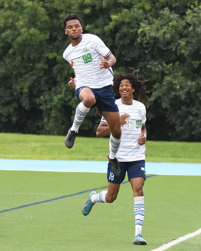 Jevontae Layne leaps in the air celebrating his goal against Blue Devils with a smiling Ijah Halley behind.